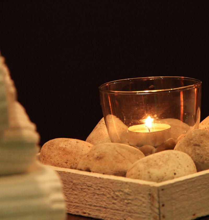 Lit candle in glass, surrounded by stones and towels.